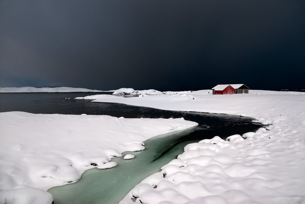 Rødt uthus i snølandskap under en mørk, stormfull himmel