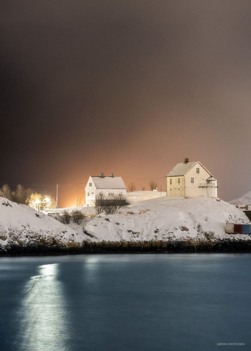 To hvite hus på en snødekt høyde om natten, med varm glød i vinduene