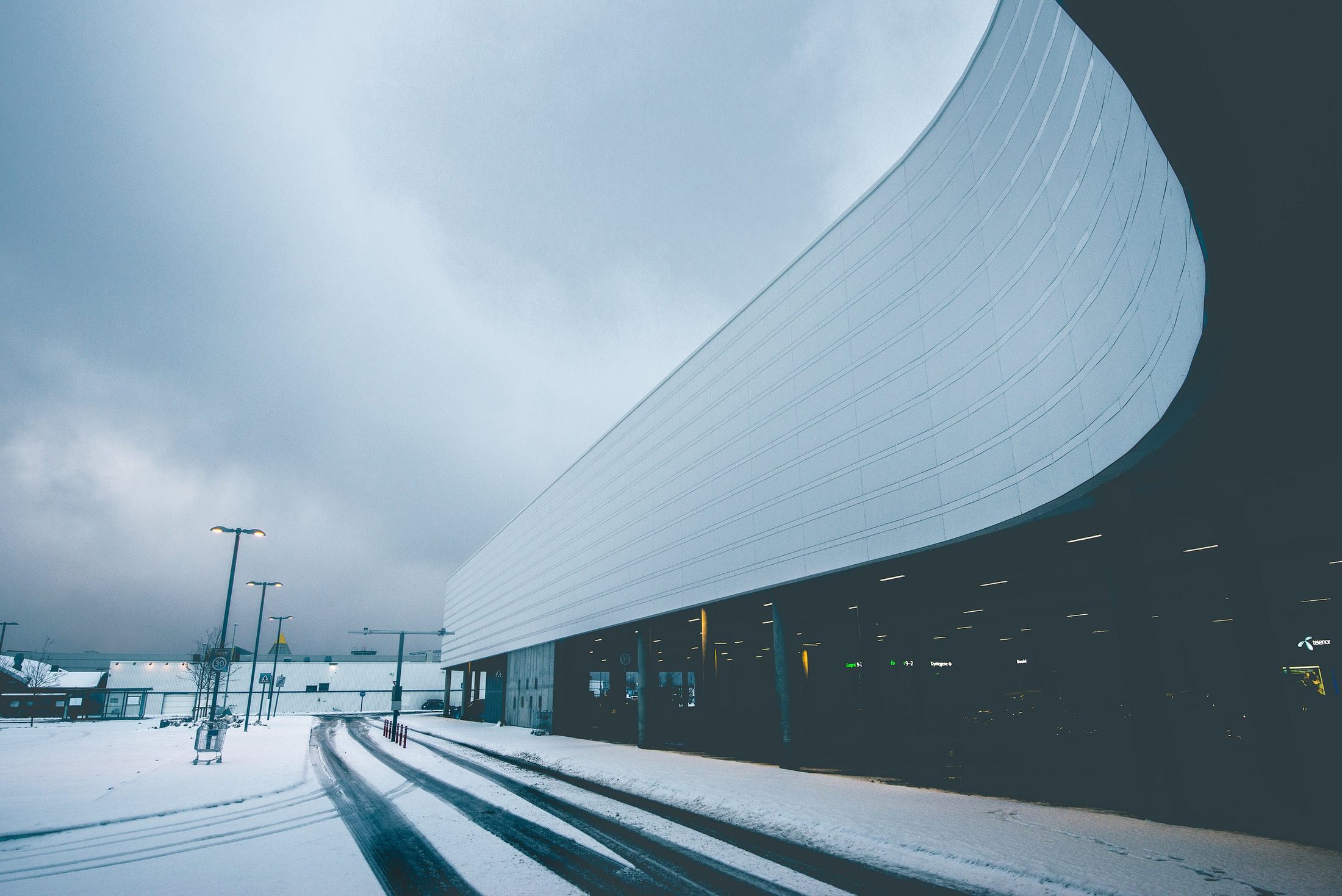 Utsikt mot et hvitt, buet bygg i vinterlys, med snø på bakken