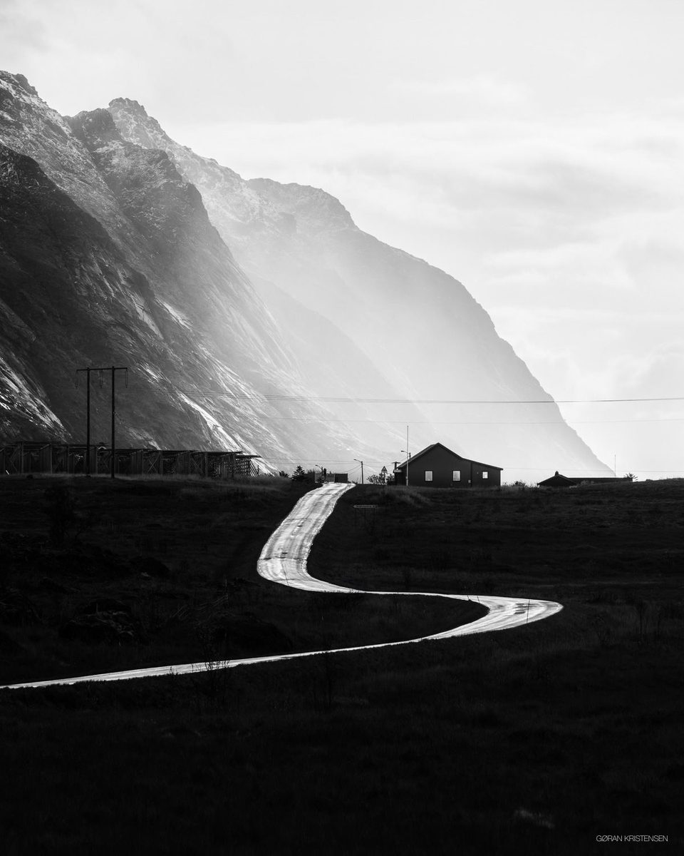 Svart-hvitt-bilde av en svingete veg som leder mot en tåkedekt fjellside