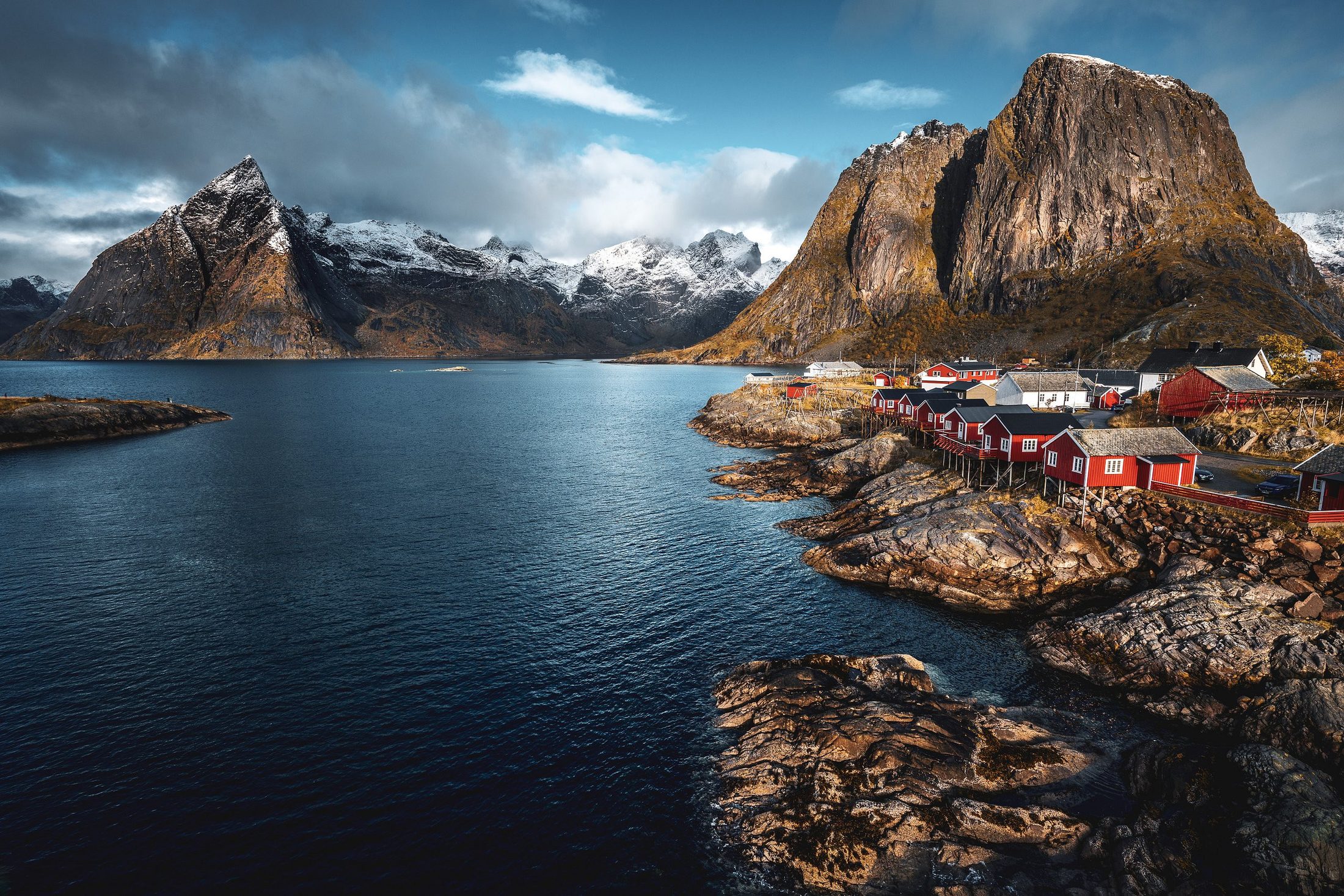 Rorbuer på svaberg ved en fjord, med bratte tinder og snødekte fjell i bakgrunnen