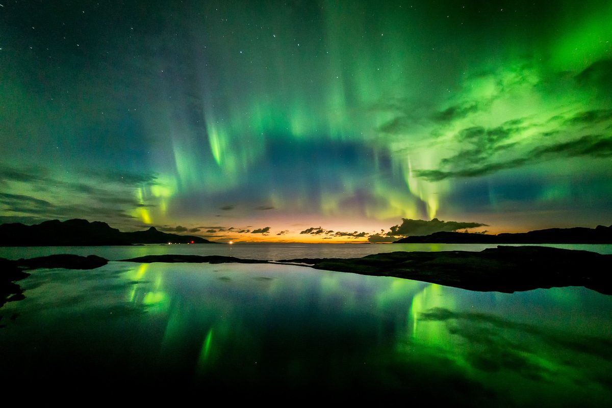 Nordlys i grønt over en kystlinje, speilet i stille vann