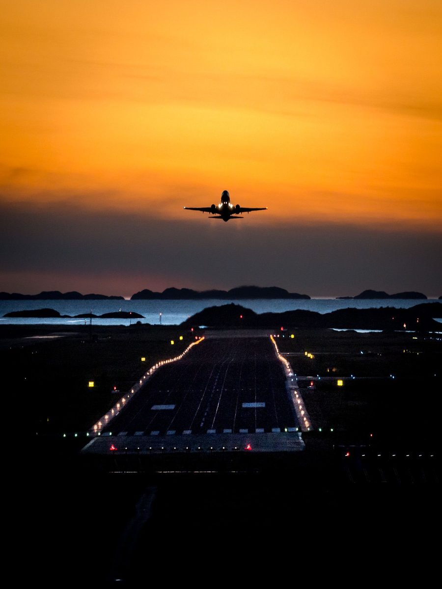 Fly som letter mot en oransje solnedgangshimmel over en rullebane